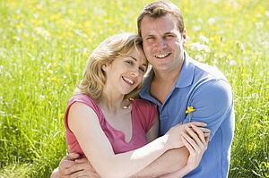 Couple sitting outdoors holding flower smiling