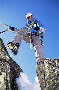 Mountain climber stepping over crevasse on mountain and smiling