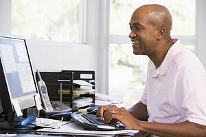 Man in home office using computer and smiling