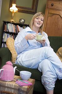 Young woman sitting on sofa at home drinking tea