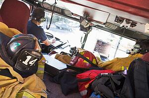 Two firefighters driving a fire engine with gear in the back (selective focus)