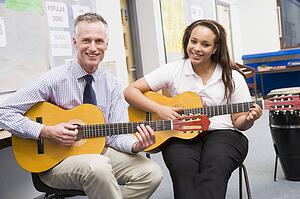 Female student receiving guitar lesson from teacher in classroom