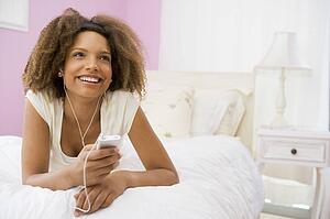 Teenage Girl Lying On Bed Using Mp3 Player