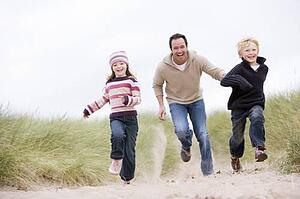Father and two young children running at beach smiling