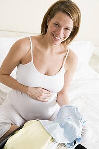 Pregnant woman packing baby clothing in suitcase smiling