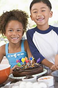 Two children in kitchen with birthday cake smiling