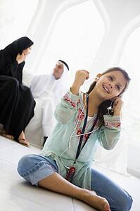 Daughter in living room listening to MP3 player and smiling with parents in background (high key/selective focus)
