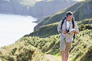 Man walking on cliffside path looking at map