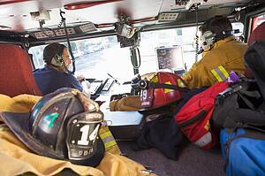 Two firefighters driving a fire engine with gear in the back (selective focus)