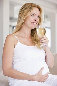Pregnant woman with glass of white wine smiling