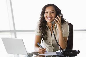 Businesswoman in office on telephone by laptop smiling (high key/selective focus)