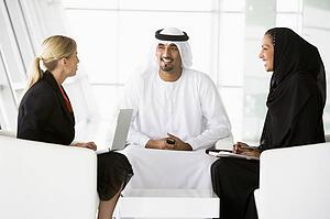 Three businesspeople indoors with a laptop and cellular phone talking and smiling (high key/selective focus)