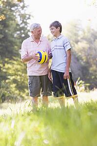 Grandfather and grandson at a park holding a ball and smiling