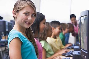 Six children at computer terminals with teacher in background (depth of field/high key)