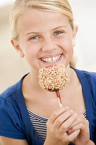 Young girl indoors eating candy apple smiling