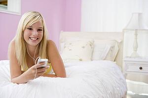 Teenage Girl Lying On Bed Using Mp3 Player