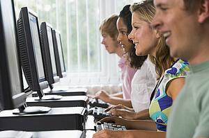 Four people sitting at computer terminals (selective focus)