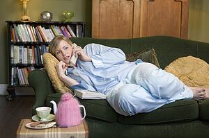 Young woman lying on sofa at home talking on telephone