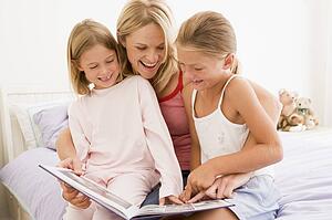 Woman and two young girls in bedroom reading book and smiling