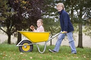 Young boy outdoors pushing young girl in wheelbarrow and smiling (selective focus)