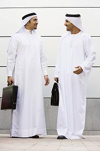 Two businessmen standing outdoors with briefcases talking and smiling