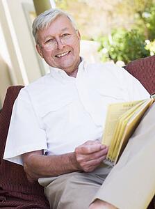 Senior woman sitting outdoors on a chair reading a book