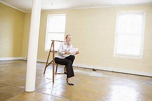 Woman sitting on ladder in empty space holding paper smiling
