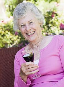 Senior woman sitting outdoors on a chair with a glass of red wine