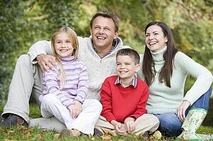 Family sitting outdoors in park smiling (selective focus)