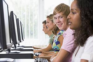 Four people sitting at computer terminals (selective focus/high key)