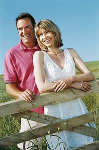 Couple standing outdoors by fence smiling