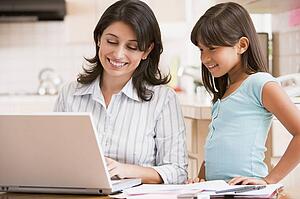 Woman and young girl in kitchen with laptop and paperwork smiling