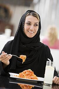 Woman at restaurant eating spaghetti and smiling (selective focus)