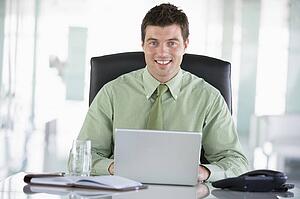 Businessman sitting in office with personal organizer using laptop smiling