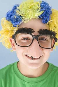 Young boy wearing clown wig and fake nose smiling