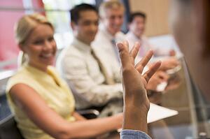 Five businesspeople at boardroom table with focus on businessman's hand
