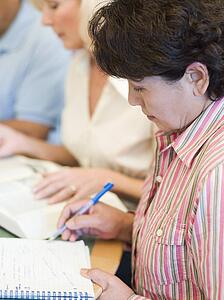 Three people in library with books and notepads (selective focus)