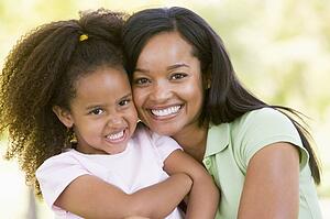 Woman and young girl outdoors embracing and smiling