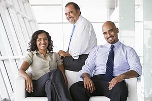 Three businesspeople sitting indoors smiling (high key/selective focus)