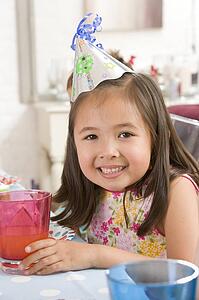 Young girl wearing party hat at table smiling