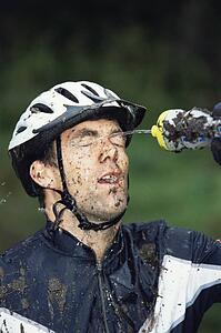 Man outdoors wearing bicycle helmet and splashing water on face (selective focus)