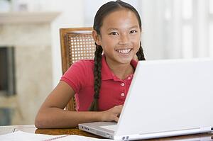 Young girl with laptop in dining room smiling