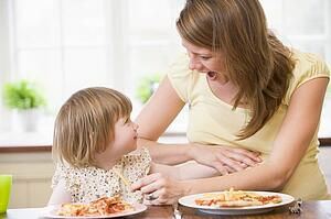 Pregnant mother with daughter touching belly eating French fries and pizza