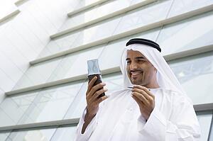 Businessman standing outdoors by building using personal digital assistant and smiling (selective focus)