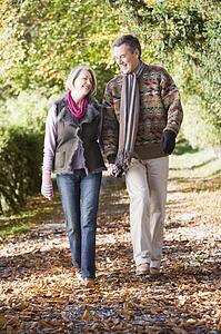 Couple outdoors walking on path in park holding hands and smiling (selective focus)