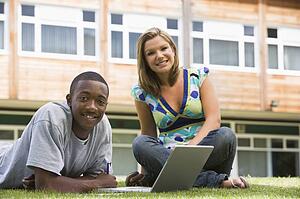 Two students outdoors on lawn with laptop