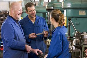 Three machinists in workspace by machine talking