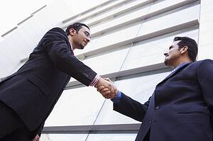 Two businessmen outdoors by building shaking hands (high key/selective focus)