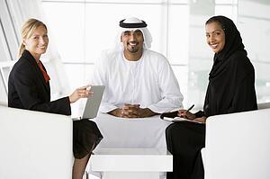 Three businesspeople indoors with a laptop smiling (high key/selective focus)