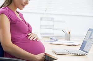 Pregnant woman at work with laptop holding belly and smiling